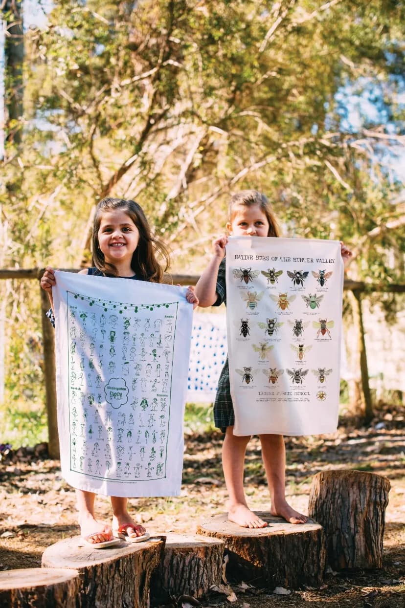 Two children holding up their school’s printed tea towels